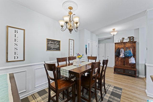 dining area with a wainscoted wall, a decorative wall, visible vents, a chandelier, and light wood-type flooring