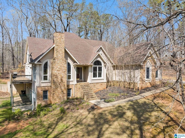 view of front of home with stairs, stucco siding, roof with shingles, and a chimney