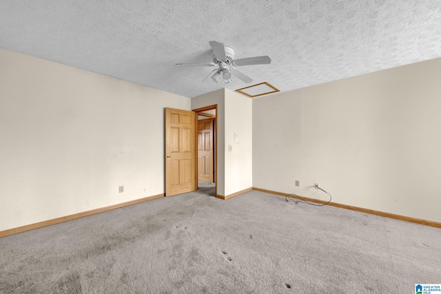 unfurnished bedroom with attic access, carpet, baseboards, a textured ceiling, and a ceiling fan