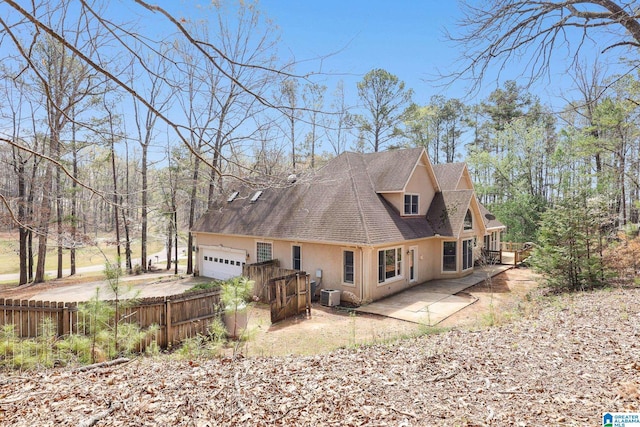 back of house with cooling unit, concrete driveway, fence, roof with shingles, and an attached garage
