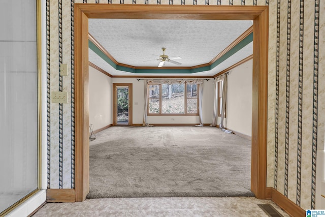 carpeted spare room featuring ornamental molding, a textured ceiling, a raised ceiling, visible vents, and ceiling fan