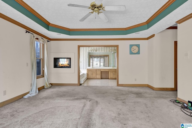 unfurnished living room with a textured ceiling, a tray ceiling, carpet, and crown molding