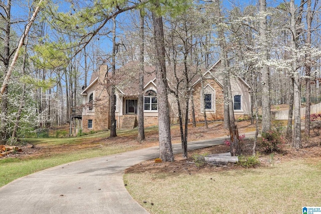 view of front of house featuring a chimney, brick siding, concrete driveway, and a front lawn