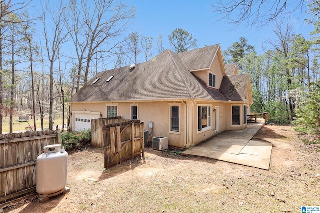 rear view of property featuring roof with shingles, stucco siding, fence, a patio, and central AC