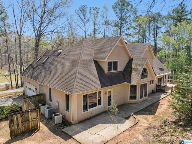 rear view of house featuring stucco siding, an attached garage, central AC, and roof with shingles