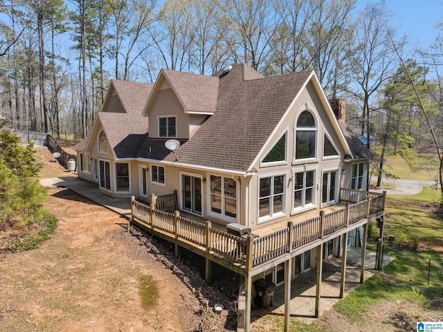 rear view of house with stucco siding, a shingled roof, a deck, and a patio
