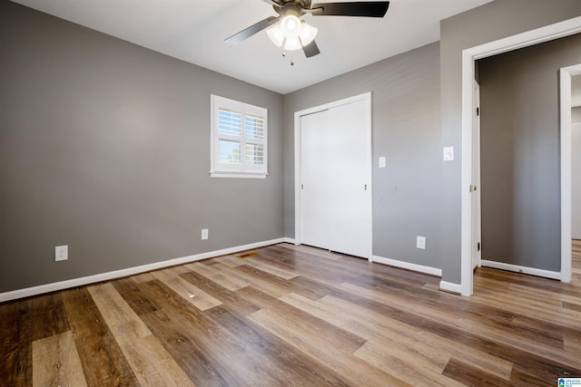unfurnished bedroom featuring baseboards, wood finished floors, a closet, and a ceiling fan