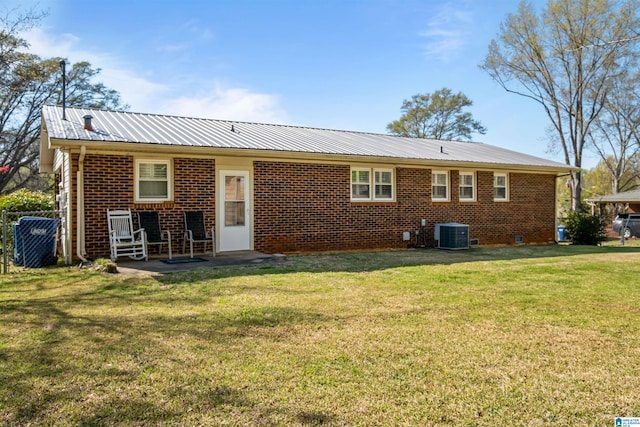 back of house featuring a lawn, metal roof, cooling unit, and brick siding