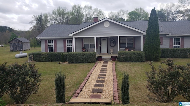 view of front of property featuring a porch, a front yard, a chimney, a storage shed, and roof with shingles