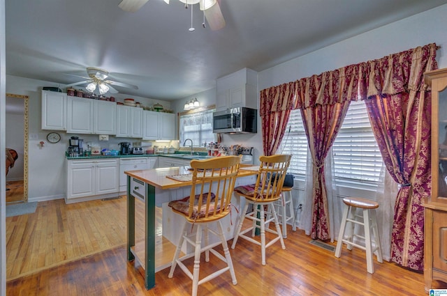 kitchen featuring stainless steel microwave, a ceiling fan, white cabinets, and light wood-type flooring