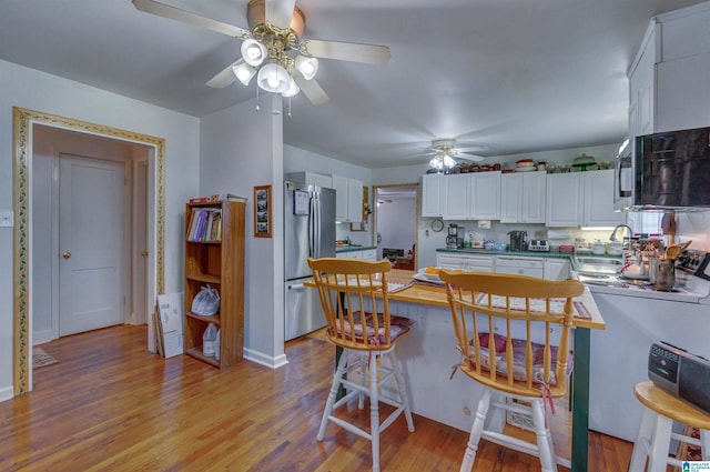 kitchen with white cabinetry, a sink, appliances with stainless steel finishes, ceiling fan, and light wood-type flooring
