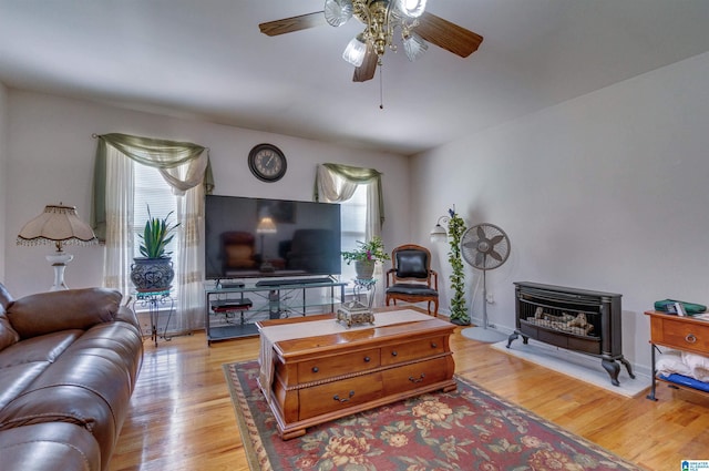 living room with a wood stove, ceiling fan, and light wood-style flooring