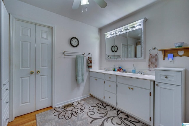 full bathroom featuring a sink, double vanity, ceiling fan, baseboards, and wood finished floors