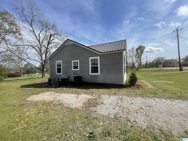 view of side of property featuring a lawn, metal roof, and cooling unit