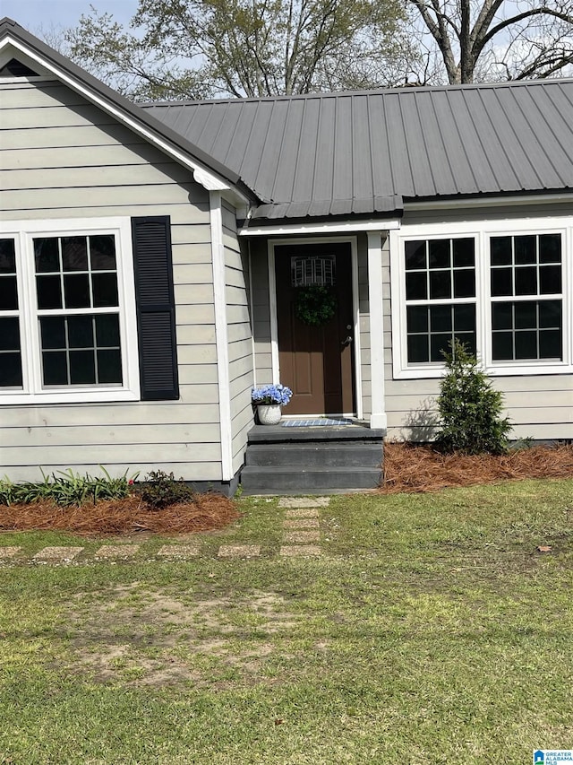 view of exterior entry with a lawn and metal roof