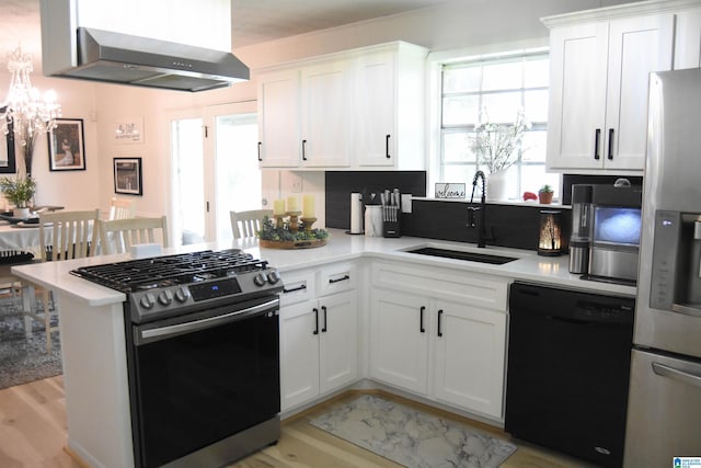 kitchen featuring a sink, wall chimney exhaust hood, appliances with stainless steel finishes, a peninsula, and an inviting chandelier