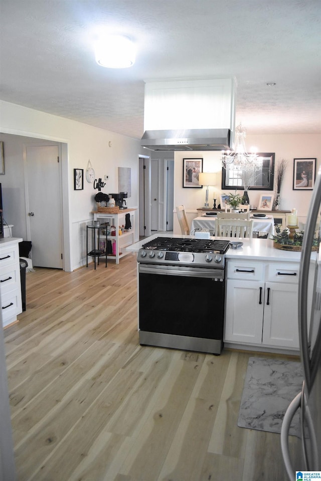kitchen with a chandelier, wall chimney exhaust hood, stainless steel appliances, white cabinets, and light wood-style floors