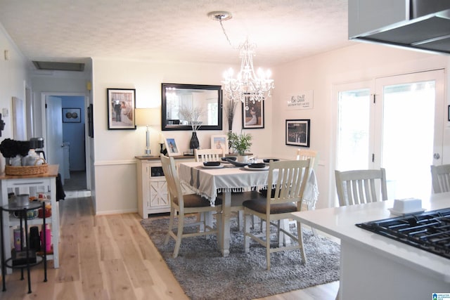 dining room featuring baseboards, a textured ceiling, an inviting chandelier, and light wood-type flooring