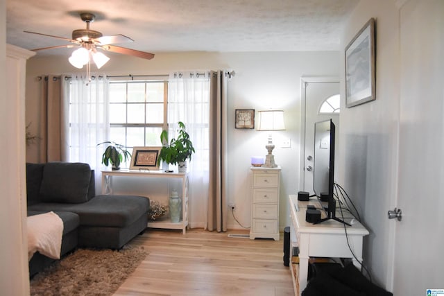 living area featuring a textured ceiling, light wood-style floors, and a ceiling fan