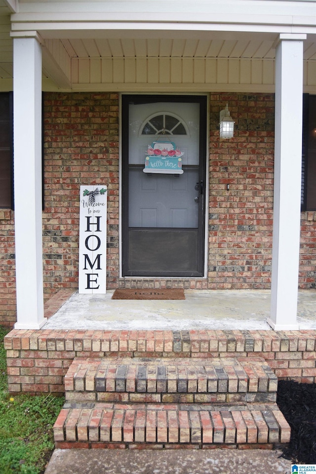 view of exterior entry featuring covered porch and brick siding
