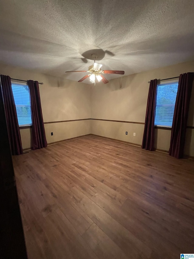 empty room with ceiling fan, plenty of natural light, wood finished floors, and a textured ceiling