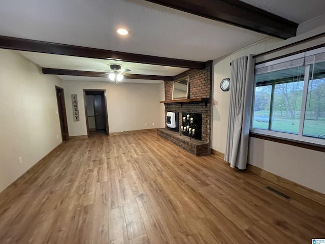 unfurnished living room with baseboards, a fireplace, visible vents, beam ceiling, and light wood finished floors