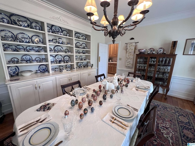 dining space featuring ornamental molding, a wainscoted wall, a decorative wall, a notable chandelier, and wood finished floors