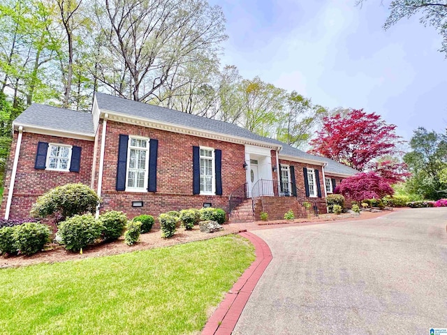 ranch-style home featuring brick siding, a front yard, and roof with shingles