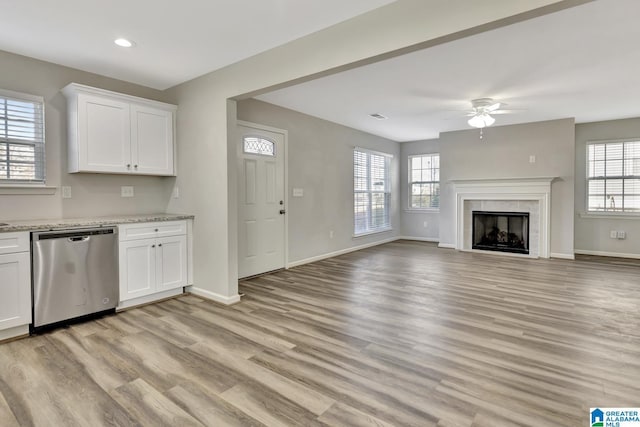 unfurnished living room featuring baseboards, light wood-style floors, a ceiling fan, and plenty of natural light