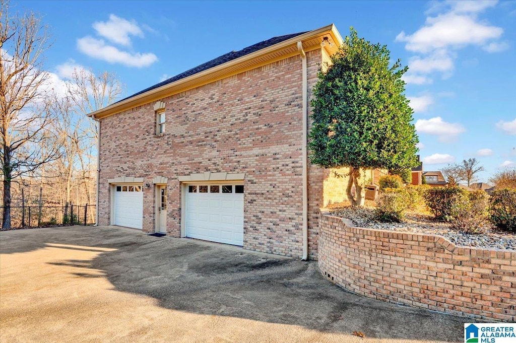 view of side of home featuring fence, driveway, an attached garage, and brick siding
