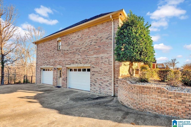 view of side of home featuring fence, driveway, an attached garage, and brick siding
