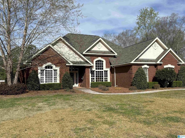 traditional-style home featuring a front lawn, brick siding, and roof with shingles