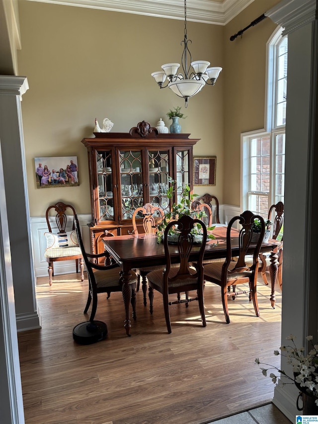 dining room featuring a wainscoted wall, wood finished floors, ornamental molding, and a chandelier