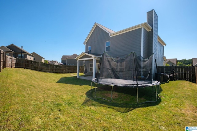 back of house with a trampoline, a fenced backyard, a chimney, and a lawn