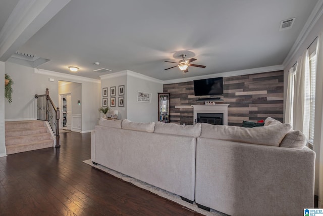 living area with visible vents, a ceiling fan, dark wood finished floors, crown molding, and stairway
