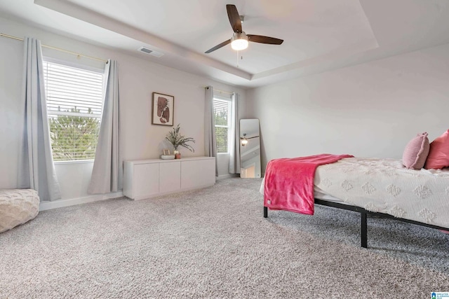 bedroom with baseboards, a raised ceiling, carpet floors, visible vents, and a ceiling fan