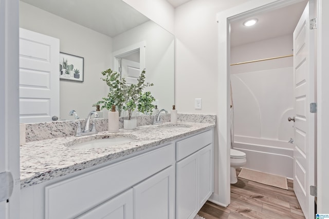 bathroom featuring double vanity, wood finished floors, toilet, and a sink