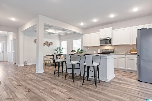 kitchen with light wood finished floors, white cabinets, a kitchen breakfast bar, and appliances with stainless steel finishes