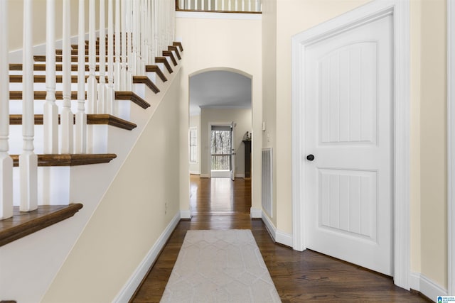 hall featuring baseboards, arched walkways, stairs, and dark wood-style flooring