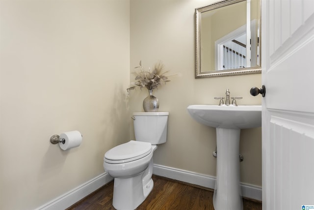 half bathroom featuring baseboards, wood finished floors, toilet, and a sink