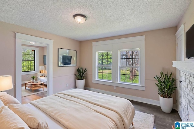 bedroom with baseboards, a textured ceiling, wood finished floors, and a fireplace