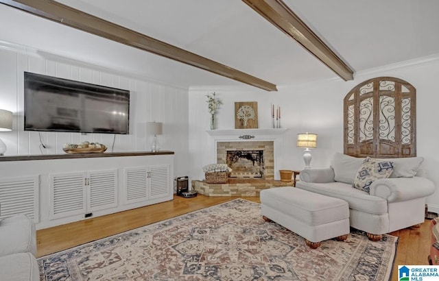 living room featuring ornamental molding, wood finished floors, beamed ceiling, and a stone fireplace