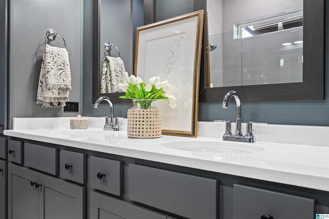 bathroom featuring double vanity, a tile shower, and a sink