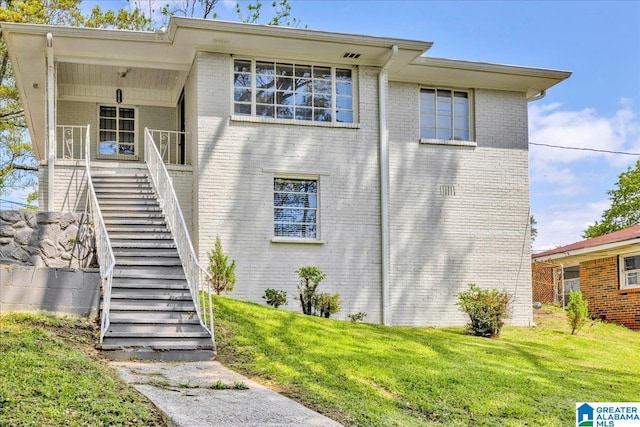 view of front of property with brick siding, stairway, and a front yard