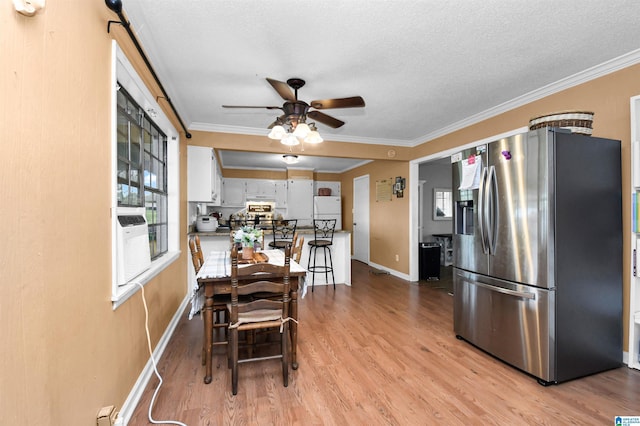 dining area featuring a textured ceiling, crown molding, baseboards, a ceiling fan, and light wood-type flooring
