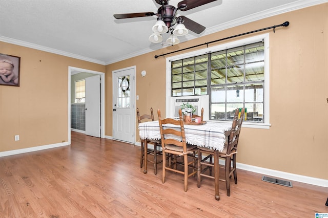 dining area featuring light wood-style flooring, a wealth of natural light, visible vents, and crown molding