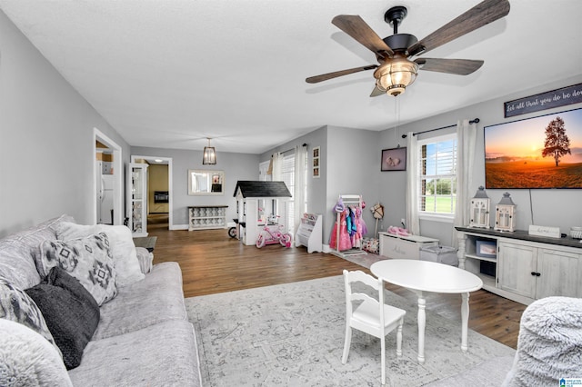 living area featuring baseboards, dark wood-type flooring, and a ceiling fan