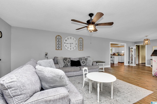 living room with baseboards, a textured ceiling, wood finished floors, and a ceiling fan