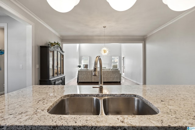 kitchen featuring pendant lighting, ornamental molding, a sink, and light stone counters