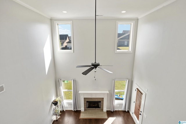 living area with a fireplace with flush hearth, dark wood-style flooring, a ceiling fan, and ornamental molding